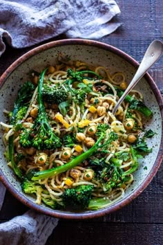 a bowl filled with noodles, broccoli and chickpeas on top of a wooden table