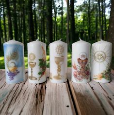 four candles with different designs on them sitting on a table in front of some trees