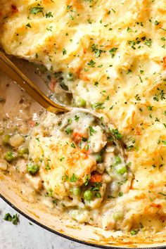 a casserole dish filled with chicken, peas and gravy topped with a spoon