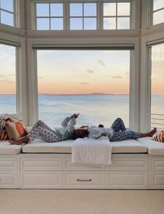 two people are lounging on a window sill in front of an ocean view