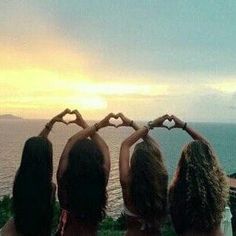 three girls are standing in front of the ocean with their hands shaped like heart shapes