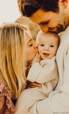 a man and woman holding a baby in their arms while they are kissing each other