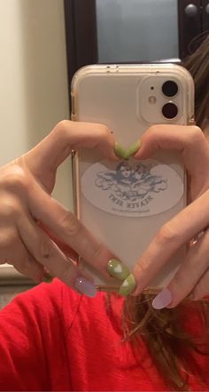 a woman making a heart shape with her hands while holding an iphone in front of her face