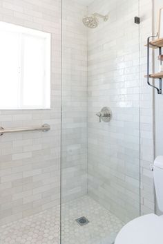 a white tiled bathroom with a shower and toilet