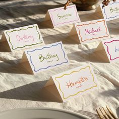 place cards with names on them sitting on a white table cloth next to silverware