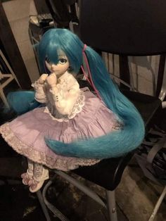 a doll sitting on top of a chair with long blue hair and wearing a dress