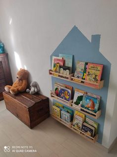 a teddy bear sitting on top of a wooden box next to a bookshelf