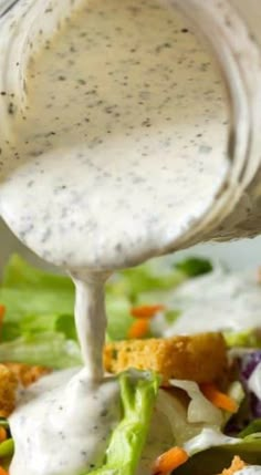 dressing being poured over a salad with lettuce and carrots