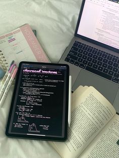 an open laptop computer sitting on top of a bed next to notebooks and books