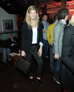 a woman standing in front of a group of people holding a purse and smiling at the camera