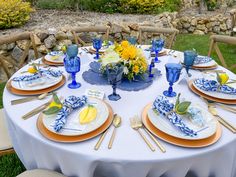 the table is set with blue and white plates, silverware, and yellow flowers