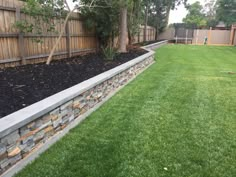 a backyard with grass, rocks and a fence