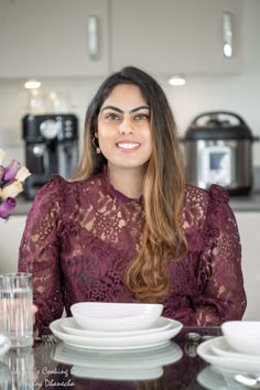 a woman sitting at a table with plates and cups in front of her, smiling