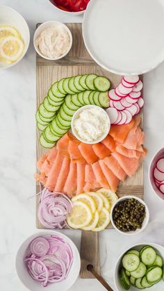 a cutting board topped with sliced up vegetables next to bowls of dips and cucumbers