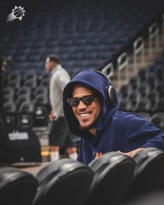 a man wearing sunglasses and a hoodie sitting in the stands at a basketball game