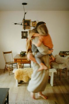 a woman holding a child in her arms while standing next to a table and chair