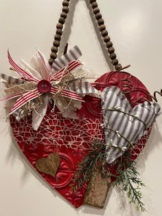 a red heart hanging on the wall with ribbons and other things attached to it's sides