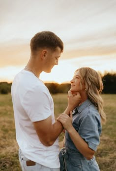 a young man and woman standing in a field looking into each other's eyes