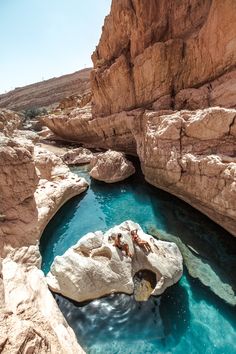 people are swimming in the blue water near some large rocks and rock formations, while another person is laying down on top of it