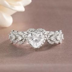 a heart shaped diamond ring sitting on top of a table next to a white rose