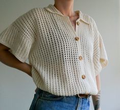 a woman with tattoos wearing a white sweater and blue denim skirt standing in front of a wall