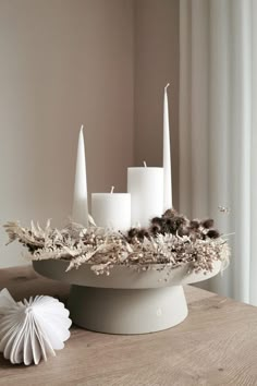 white candles and dried flowers in a bowl on a table