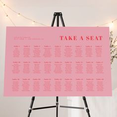 a pink wedding seating chart on a tripod in front of a string of lights