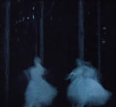 two people in white dresses are running through the dark woods at night with their faces obscured by fog