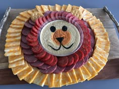 a platter with cheese, meat and crackers on it that has a lion's face painted on the side