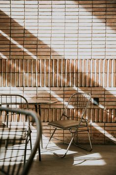 two chairs sitting next to each other in front of a brick wall with long shadows on it