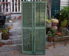 an old green shuttered door sitting on the side of a building next to potted plants