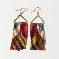 two pairs of multicolored beaded earrings hanging from hooks on a white surface