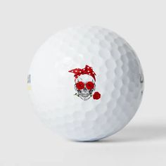 a white golf ball with a skull and red bow on it's head, in front of a gray background