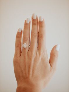 a woman's hand with a diamond ring on her left hand and white nail polish