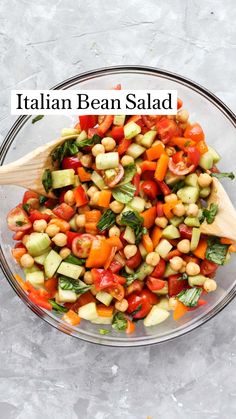 a glass bowl filled with chickpeas, tomatoes and cucumber garnish