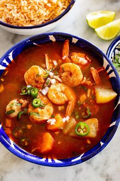 two bowls filled with shrimp and rice on top of a table next to limes