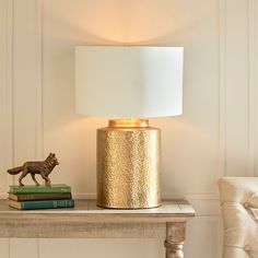 a table with a lamp, books and a cat figurine sitting on it