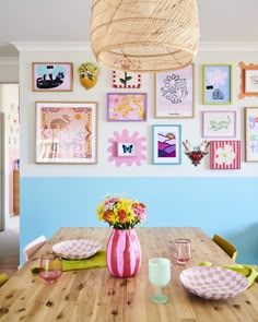 a wooden table topped with plates and vases filled with flowers next to pictures on the wall