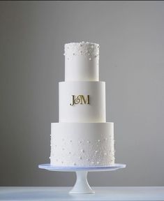 a three tiered white wedding cake with gold initials