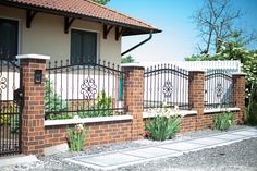 a brick fence with wrought iron bars and flowers on the top, next to a house