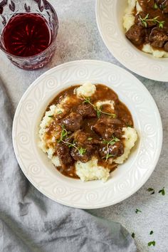 two white plates topped with meat and gravy next to a glass of wine