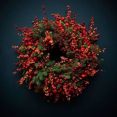 an overhead view of a wreath with red berries and green leaves on a dark background