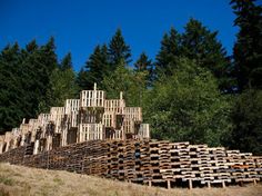 a pile of wooden pallets sitting on top of a grass covered hillside next to trees