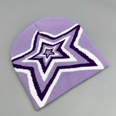 a purple and white knitted beanie with a star on the front, sitting on a gray surface