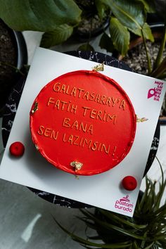 a red cake with writing on it sitting in front of some potted planters