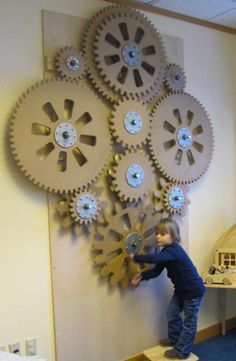 a man standing next to a large clock made out of metal gears on a wall