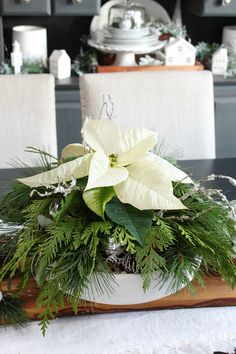 a white poinsettia and greenery in a bowl on a dining room table