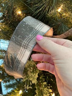 a hand holding a silver ribbon in front of a christmas tree