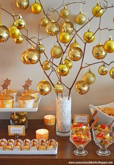 a table topped with lots of food and desserts next to a tree filled with gold ornaments