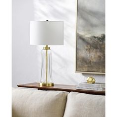 a table lamp sitting on top of a wooden table next to a white pillow and painting